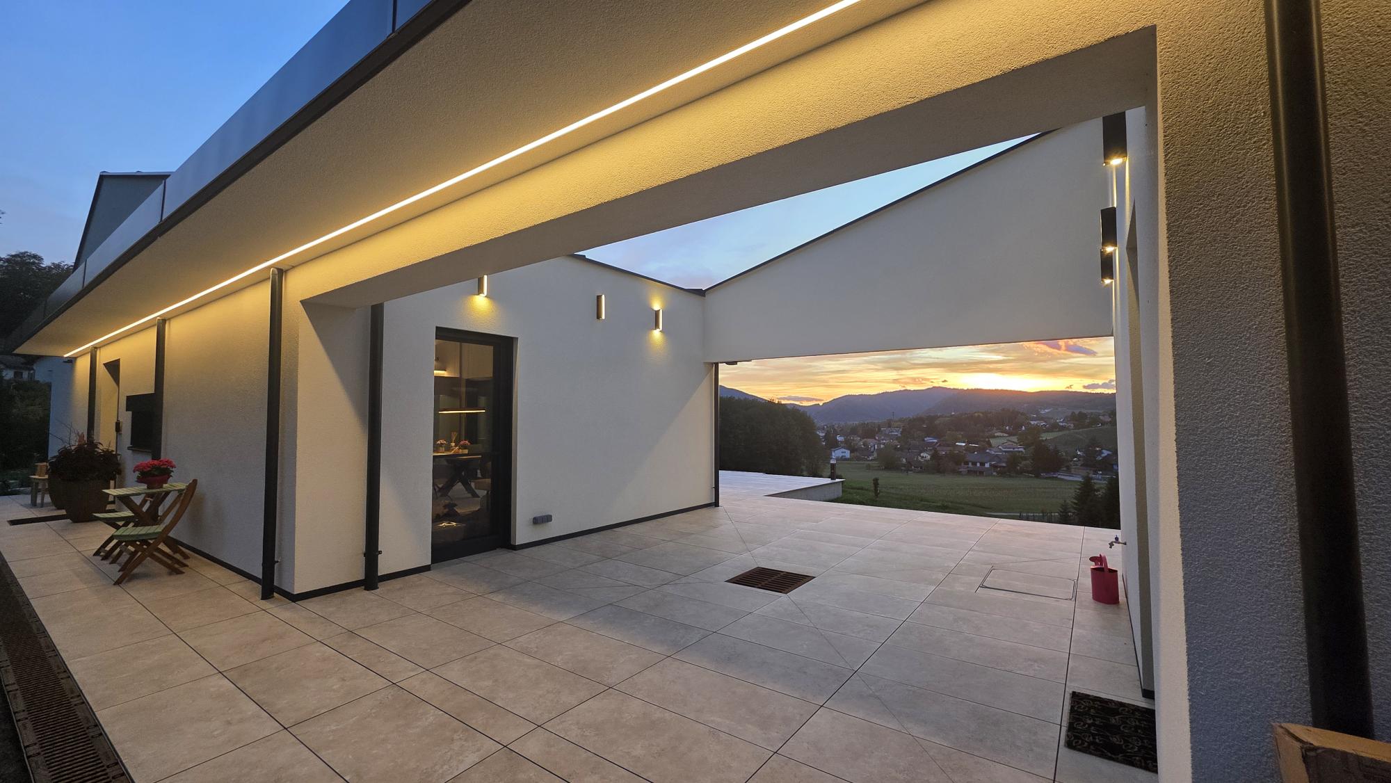 Überdachter Durchgang mit LED-Lichtband und Wandleuchten bei Sonnenuntergang – KNX-Lichtsteuerung in einem Einfamilienhaus bei Graz